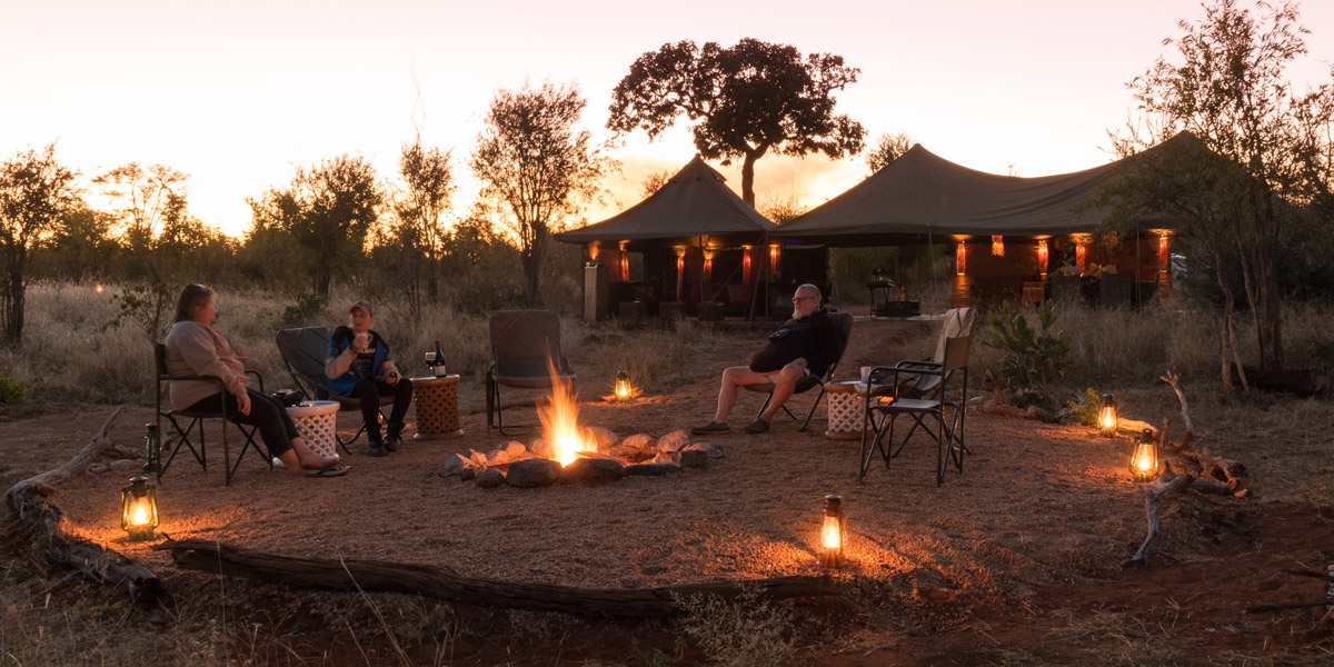 people sitting around a campfire at hwange bush camp in zimbabwe