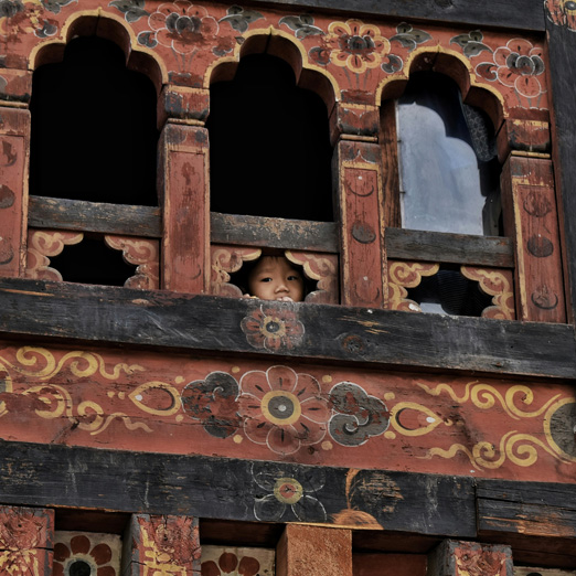 child looking through windows of traditional house in bhutan
