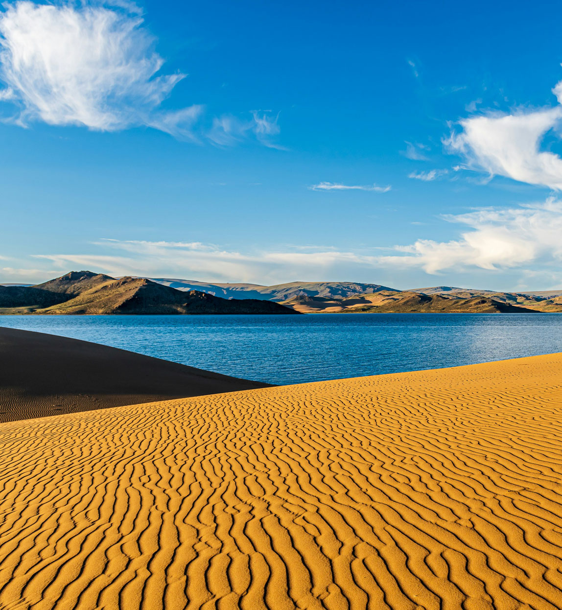 view of mongolia's desert dunes with lake in the background