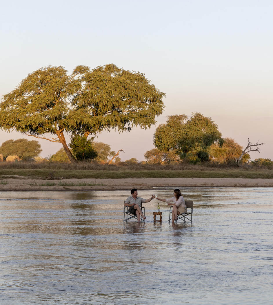 couple sat in river having sundowners in south luangwa national park