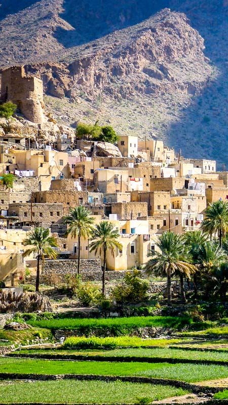The beautiful mountain village of Balad Sayt sits in front of green fields in Wadi Bani Awf, Oman