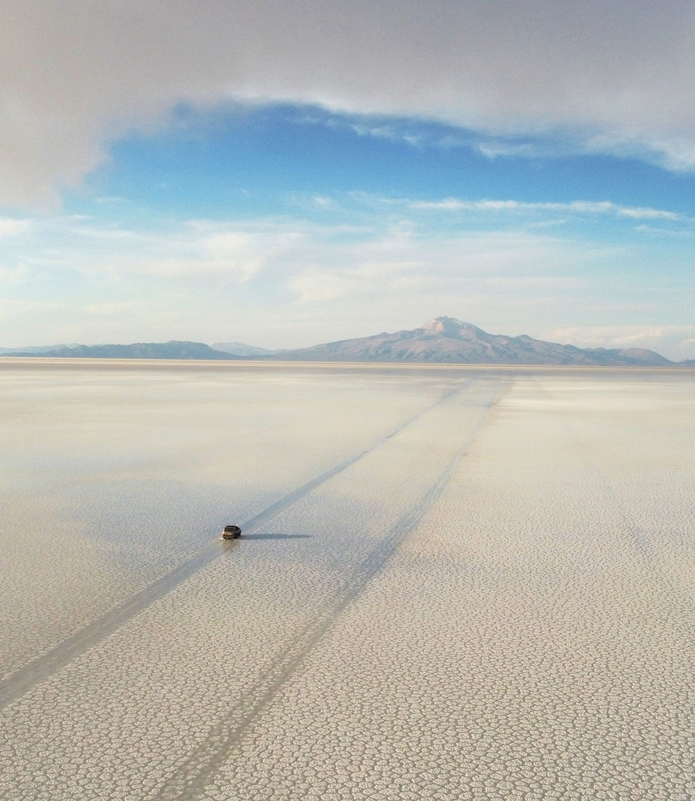 jeep driving across the uyuni salt flats in bolivia towards distant mountains