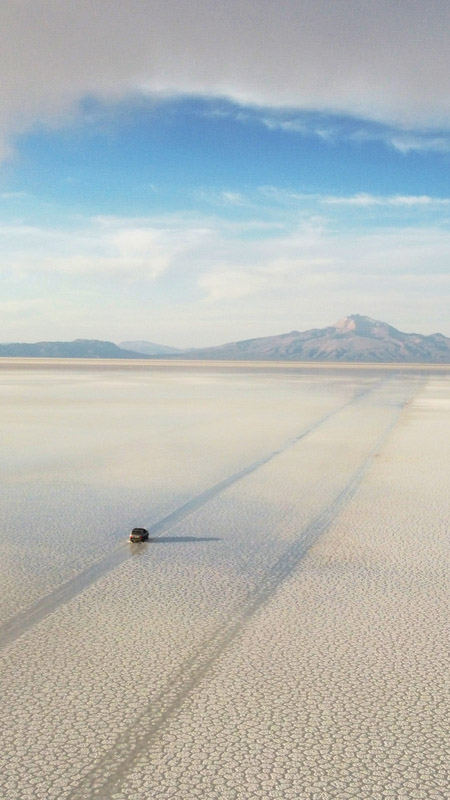 jeep driving across the uyuni salt flats in bolivia towards distant mountains