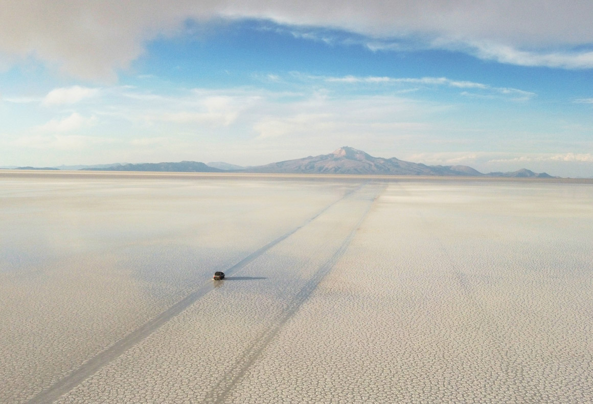jeep driving across the uyuni salt flats in bolivia towards distant mountains