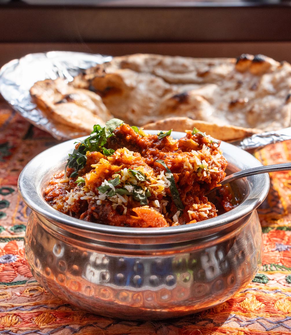 culinary dish daal maas - Lamb curry with tomatoes and fiery chili, served in a metal dish with flatbreads