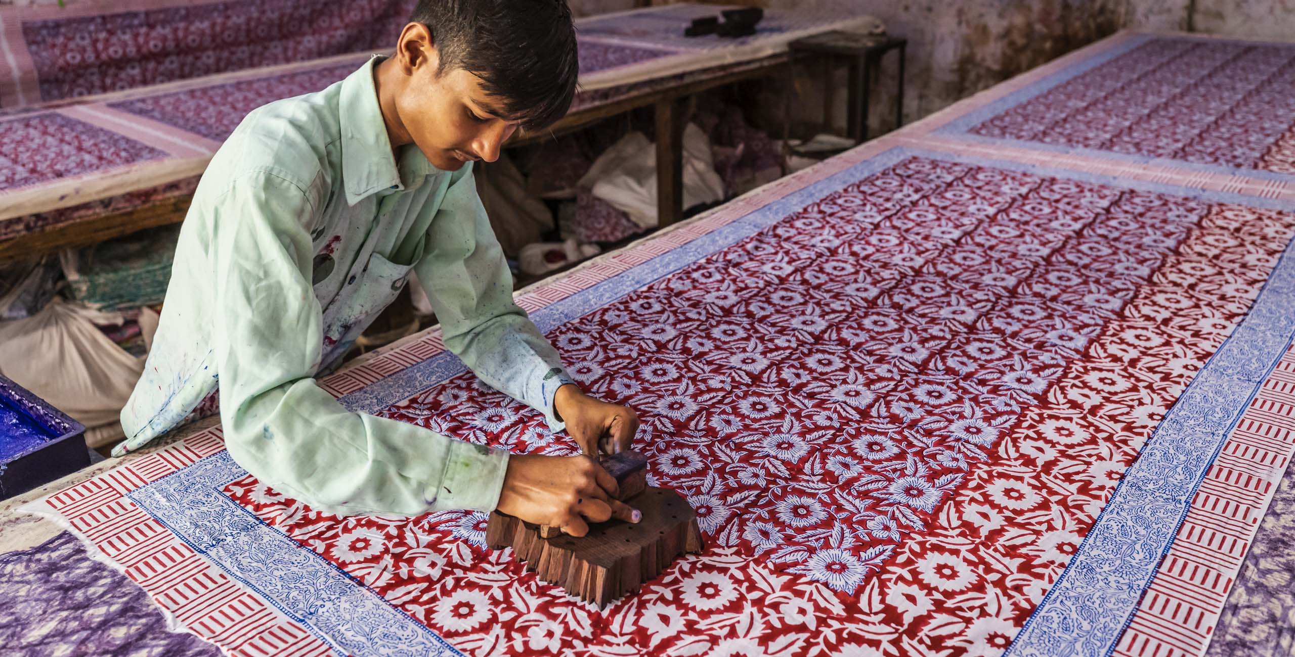 Young man working in block printing factory in Jaipur, India, Jaipur is famous for a screen and block printing. Block printing is the process of printing patterns by means of engraved wooden blocks.
