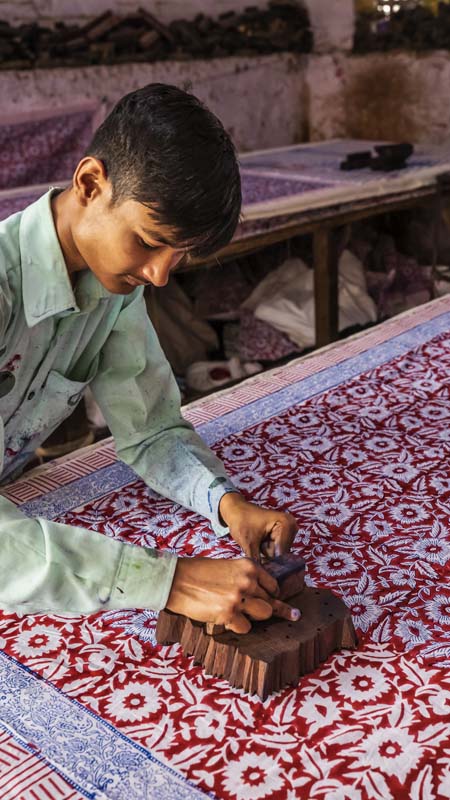Young man working in block printing factory in Jaipur, India, Jaipur is famous for a screen and block printing. Block printing is the process of printing patterns by means of engraved wooden blocks.