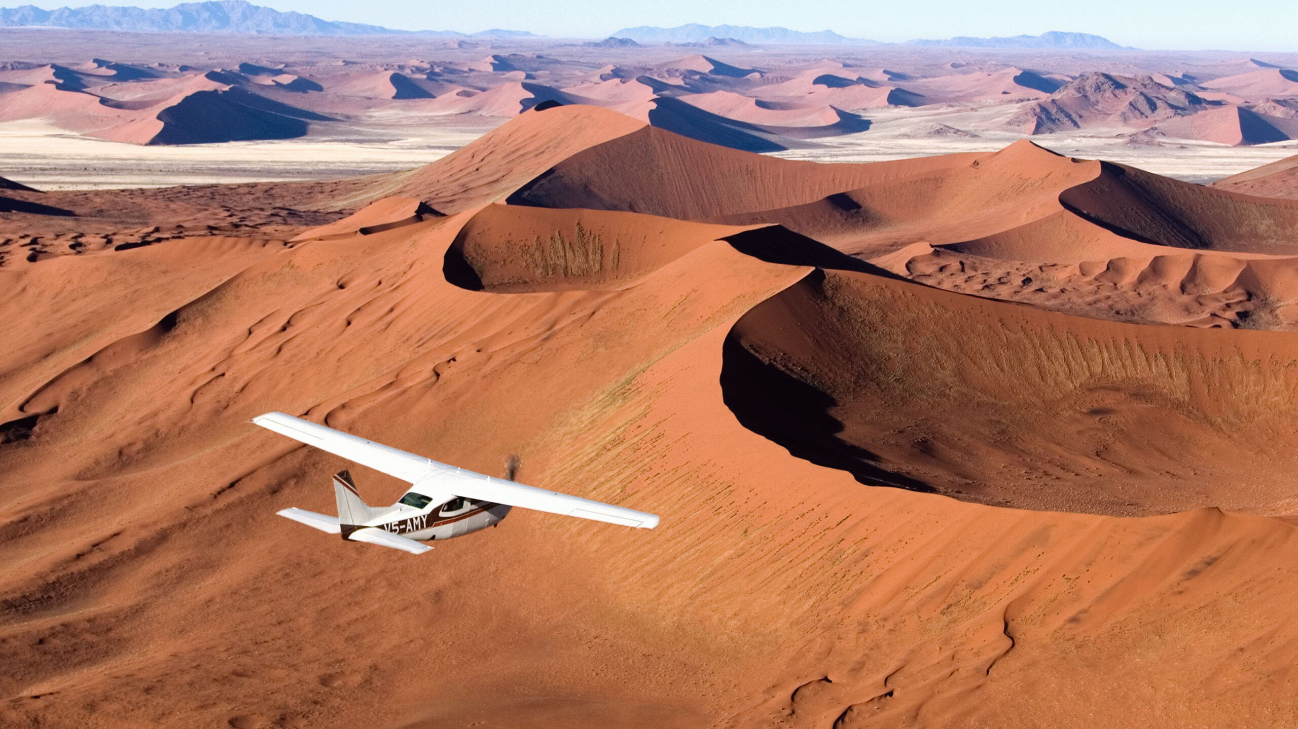 small airplane flying over the red dunes of namibia's skeleton coast