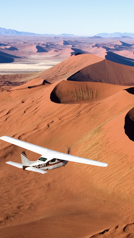small airplane flying over the red dunes of namibia's skeleton coast