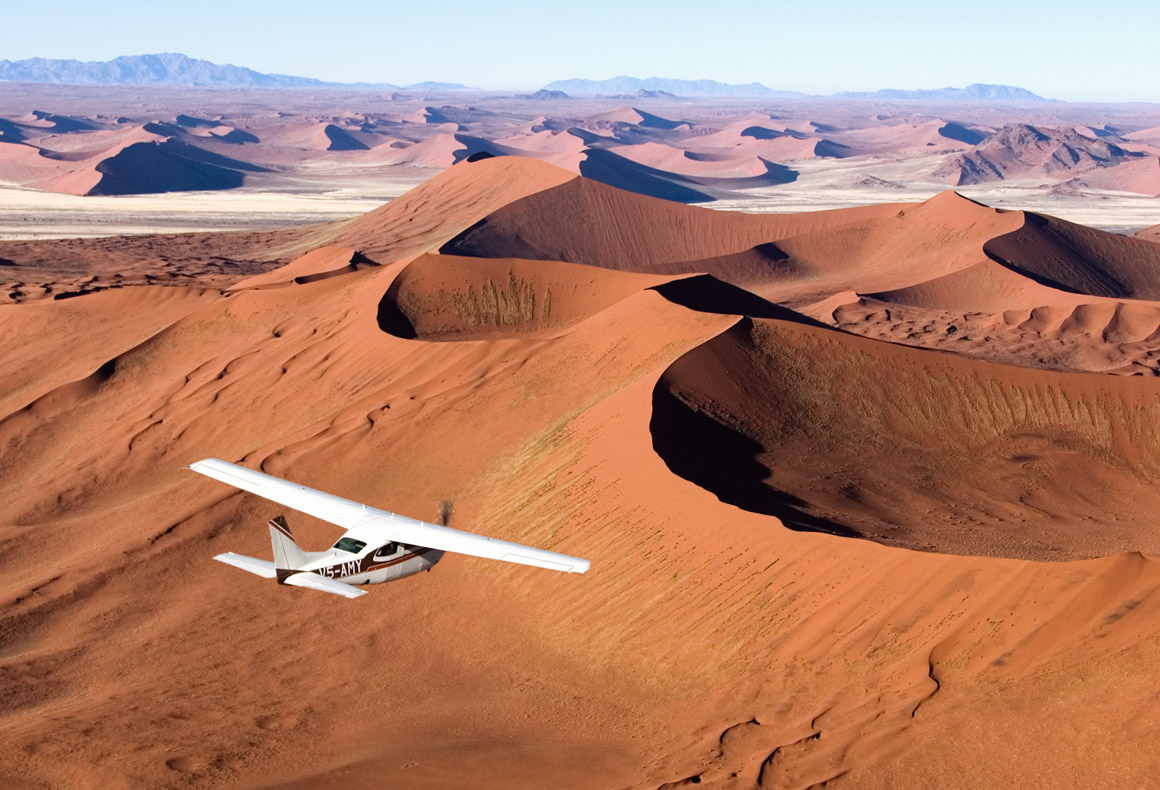 small airplane flying over the red dunes of namibia's skeleton coast