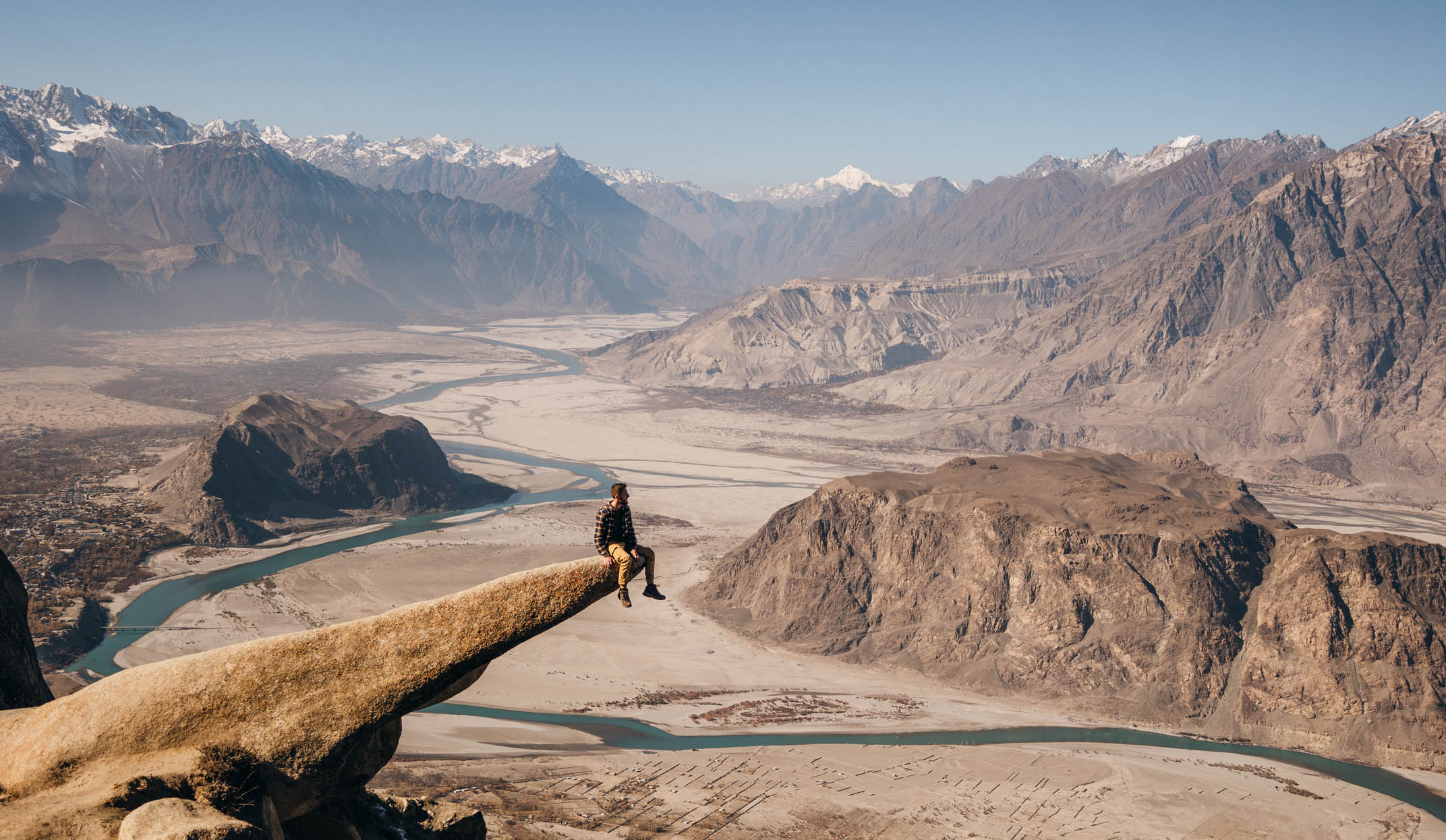 A male traveler sitting at the edge of Marsur Rock and looking at scenic view of Indus River valley in the Himalayas mountains in Pakistan