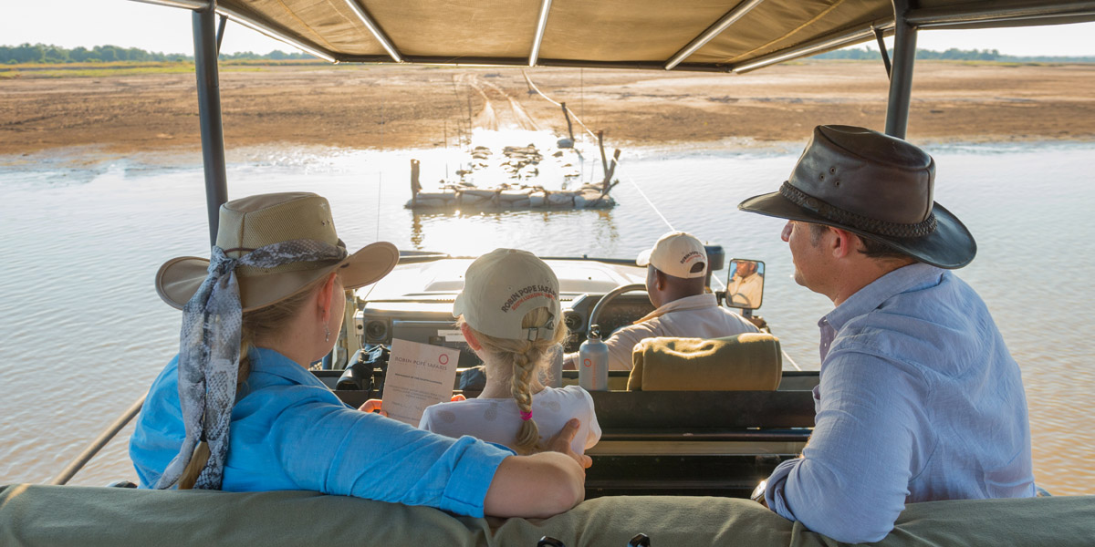 crossing a river in game drive vehicle on a family safari in zambia