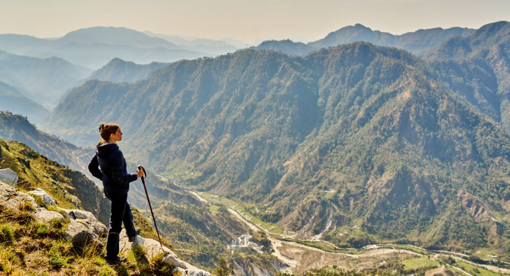 walker in indian himalayas in northern india overlooking a cliff side down into a mountain valley