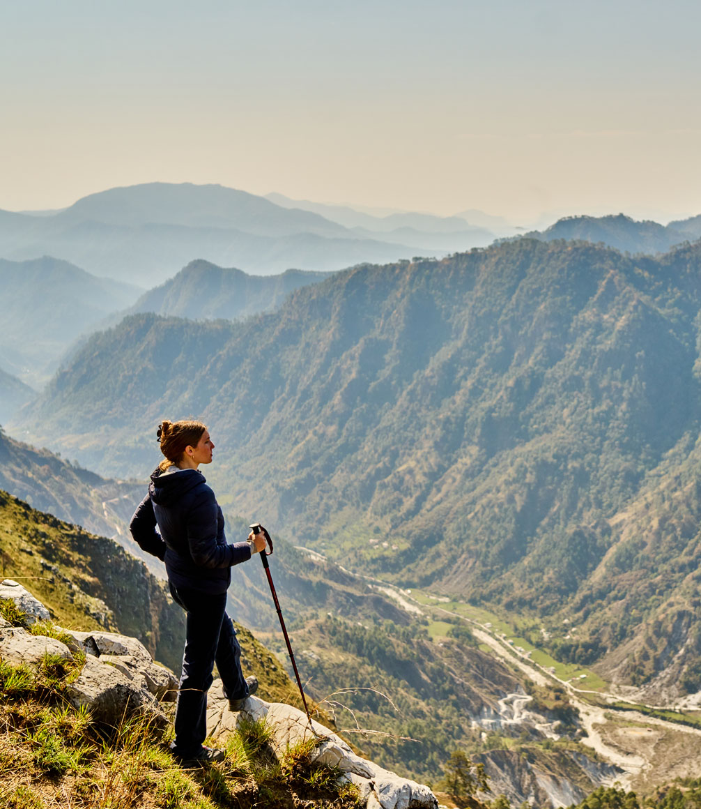 walker in indian himalayas in northern india overlooking a cliff side down into a mountain valley